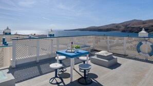 Un balcone con tavolo e sgabelli, vista su uno specchio d'acqua e colline lontane.