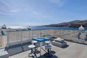 Een balkon met een tafel en krukken, met uitzicht op een waterpartij en heuvels in de verte.