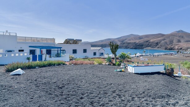 Un edificio costiero con facciata blu e bianca, una spiaggia in primo piano e montagne sullo sfondo.