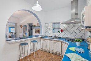 Een keuken met een blauw aanrecht, witte kastjes, een gasfornuis en een hangende lamp.