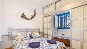 Una camera da letto con un letto, una testiera in legno, un elemento decorativo a parete, una finestra vista e una piccola pianta sul davanzale.