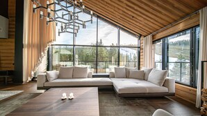 Ein modernes Wohnzimmer mit einer Eckcouch, einem Holztisch und großen Fenstern mit Blick ins Freie.