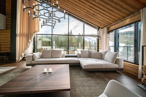 Ein modernes Wohnzimmer mit einer Eckcouch, einem Holztisch und großen Fenstern mit Blick ins Freie.