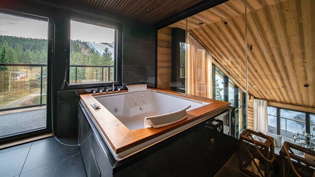 Ein modernes Badezimmer mit einer großen Holzbade Wanne, großen Fenstern und Blick ins Freie.