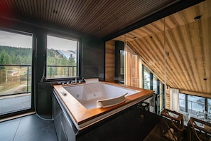 Ein modernes Badezimmer mit einer großen Holzbade Wanne, großen Fenstern und Blick ins Freie.