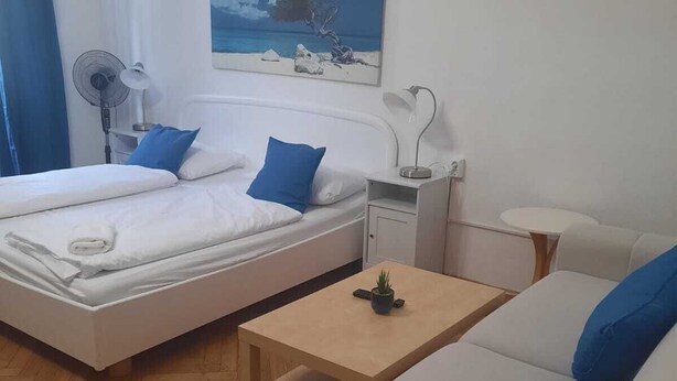 Hotellihuone, jossa on kaksi sänkyä, pieni pöytä, sohva, tuuletin ja taulu seinällä.