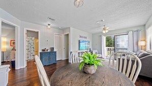 A spacious living area with a dining table, chairs, a potted plant, and a view of the outdoors. - Wolf Bay Villas 208 (Orange Beach)