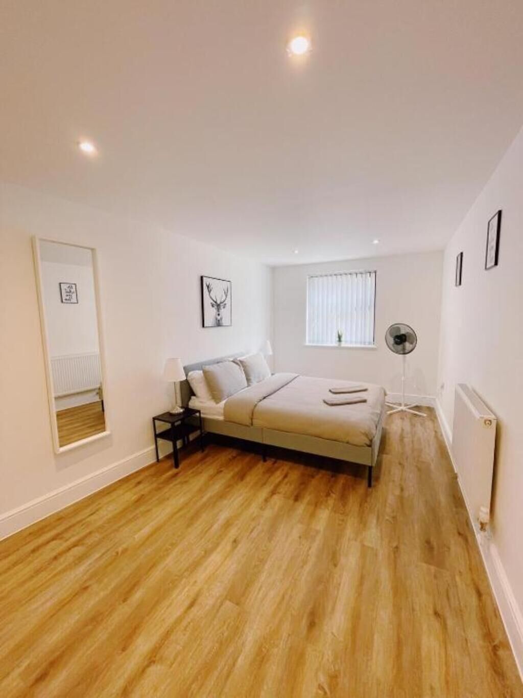 Un dormitorio con cama, mesita de noche, lámpara de pie, ventana con persianas y radiador.