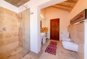 Uma casa de banho com cabine de chuveiro em vidro, lavatório branco e porta de madeira.