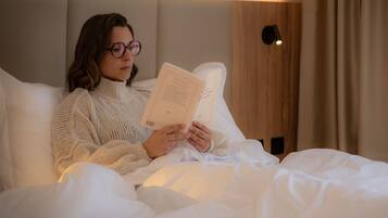 A person reading a book in a room with a bed, a wooden wall panel, and a light fixture.