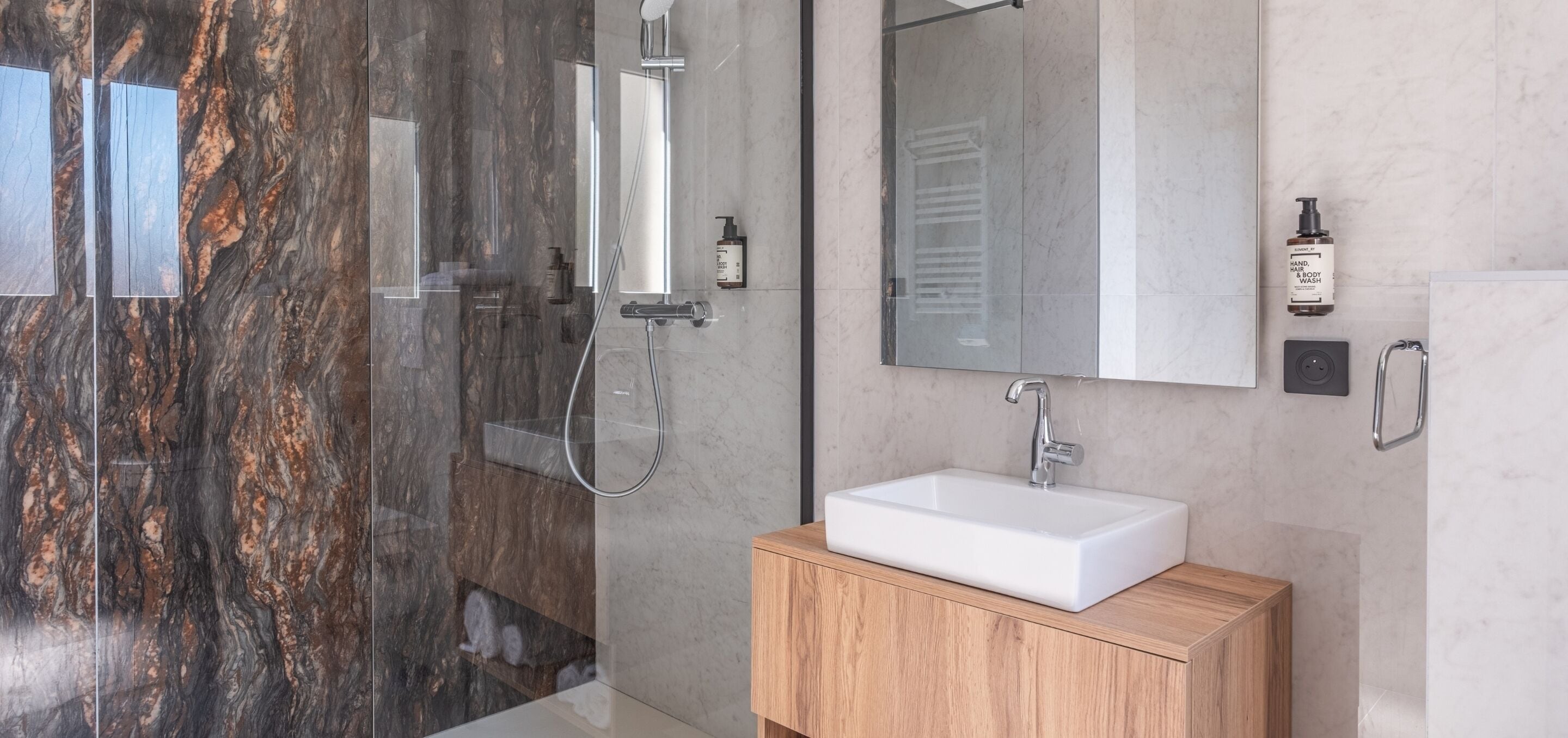 Une salle de bain moderne avec un mur en marbre, un lavabo blanc et un meuble-lavabo en bois.