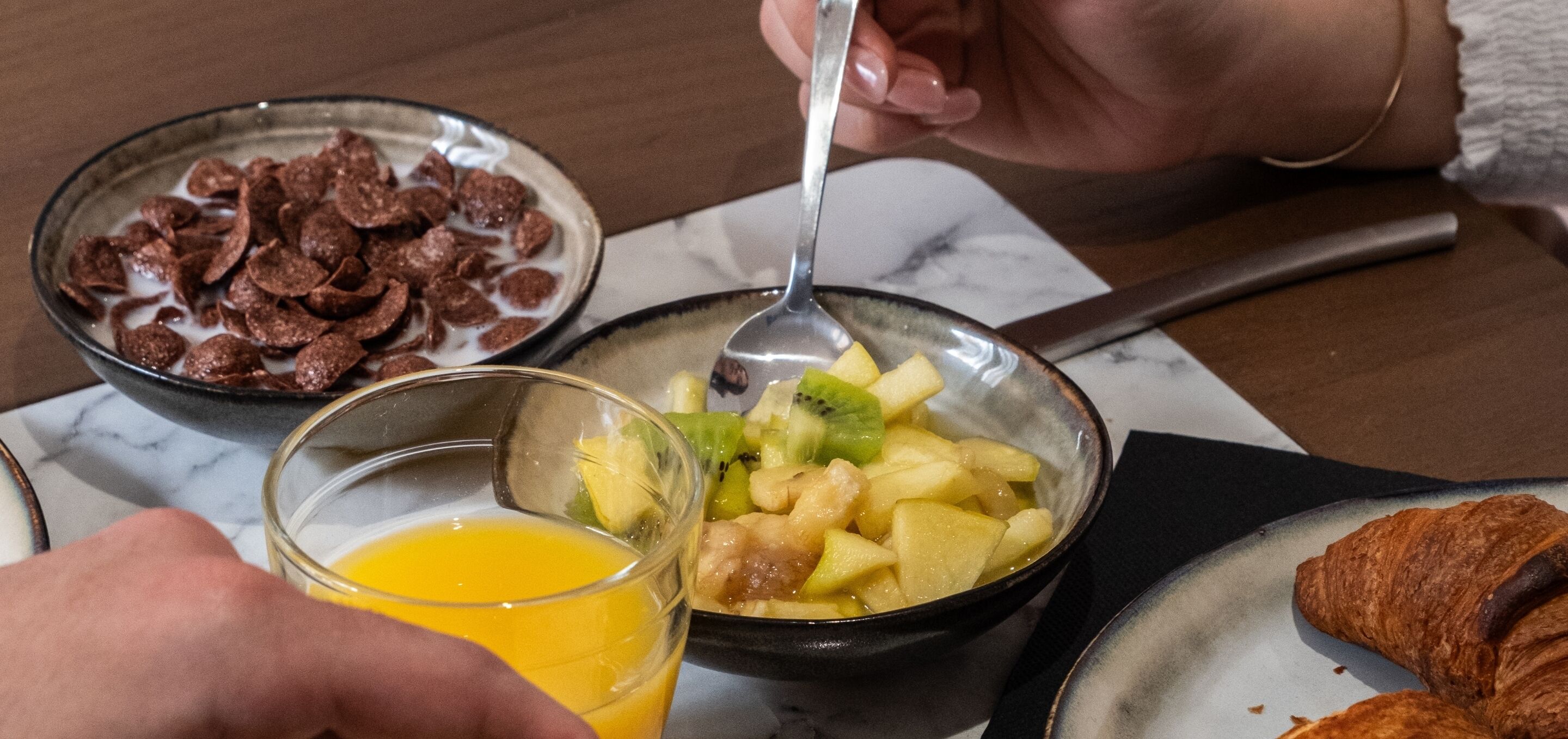 Een ontbijtje met cornflakes, fruit en een croissant op borden.