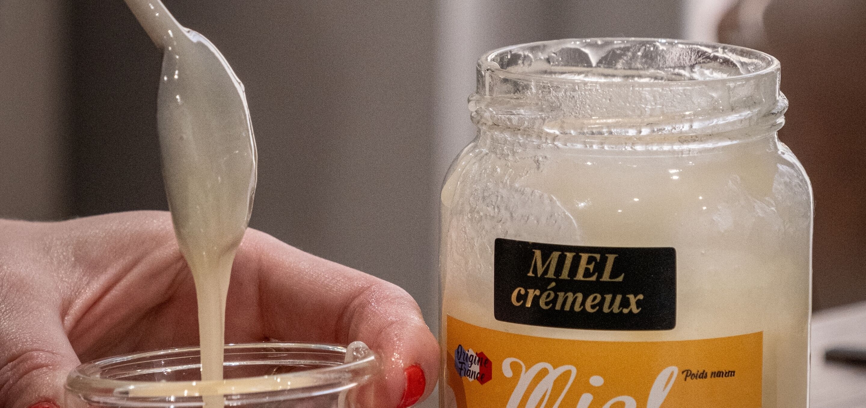 A hand holding a spoon over a jar of Miel cremeux.