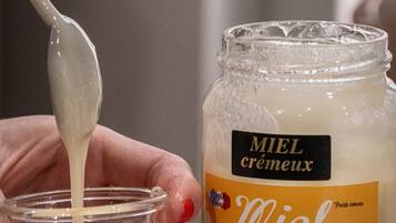 A hand holding a spoon over a jar of Miel cremeux.