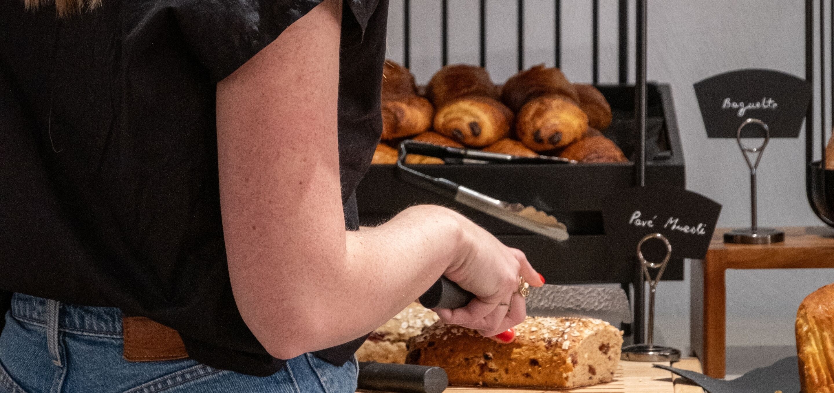 A person handling a loaf of bread with a sign labeled 'Baguette' in the background.