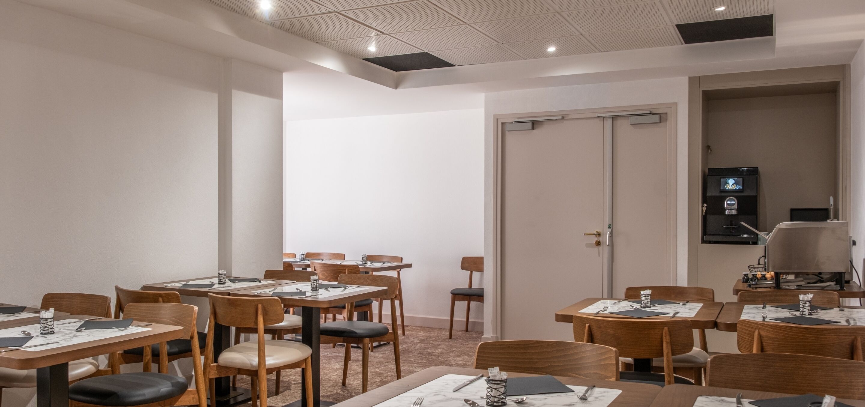 A hotel dining area with multiple tables and chairs, a door with a keypad lock, and a coffee machine.