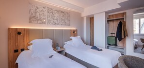 Ein Hotelzimmer mit zwei Betten, einem Holz-Kopfteil, einem an der Wand befestigten Kunstwerk, einem Kleiderständer und einem Koffer.