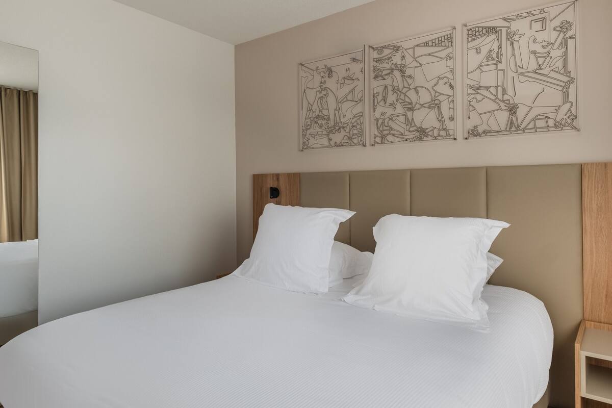 A hotel room with a large bed, a wooden headboard, a bedside table, and a mirror.