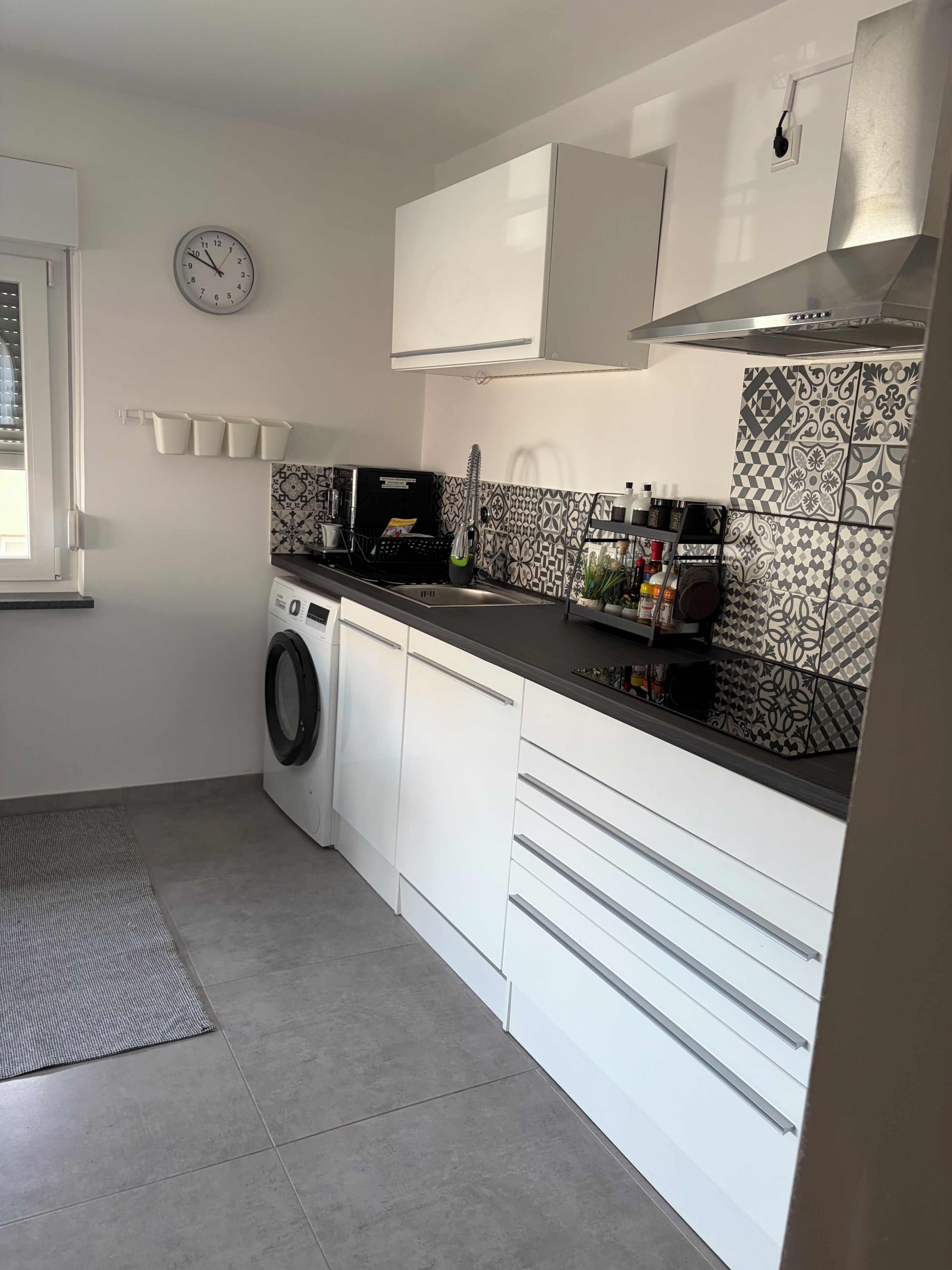 Une cuisine de taille réduite, équipée d’un lave-linge, d’une horloge et de carreaux décoratifs.