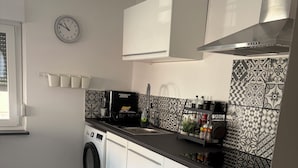 A compact kitchen with a washing machine, a clock, and patterned tiles.