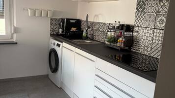 Une cuisine de taille réduite, équipée d’un lave-linge, d’une horloge et de carreaux décoratifs.