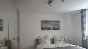 A bedroom with a bed, a wardrobe, a painting, and a window with curtains.