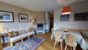 A cozy living room with a white sofa, a patterned rug, a fireplace, and a dining table with chairs. - 3-room apartment approx. (Celerina/Schlarigna)