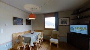 A cozy room with a dining table, chairs, a TV, and artwork on the walls. - 3-room apartment approx. (Celerina/Schlarigna)