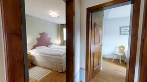 A bedroom with a large bed, a wooden headboard, a bedside table with a lamp, and a chair in the corner. - 3-room apartment approx. (Celerina/Schlarigna)