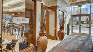 Una hall d'albergo con una reception, ampi vasi e vista sulla città attraverso grandi finestre.