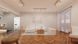 Una sala de estar moderna con piso de madera en patrón de espiga, una mesa de centro de vidrio, un sofá blanco y un ventanal con cortinas translúcidas.