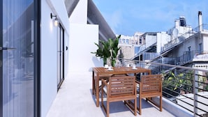 Un balcón con una mesa y sillas de madera, una planta en maceta y vistas de la ciudad.