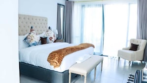 Un dormitorio de hotel moderno con una cama grande, un banco, una silla y vistas al exterior.