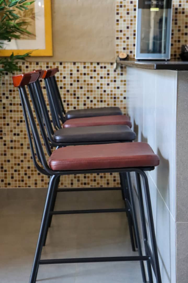 A row of three metal chairs with cushioned seats and backs, positioned against a wall with a mosaic tile pattern.