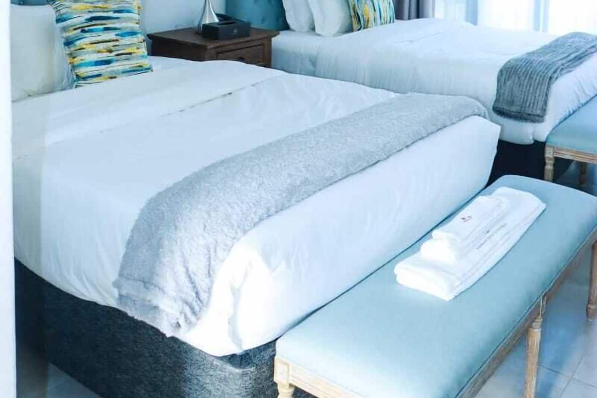 Een hotelkamer met twee bedden, een nachtkastje met een lamp en een airconditioning op de muur.