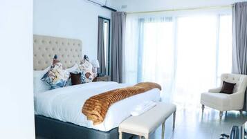 A modern hotel room with a large bed, a bench, a chair, and a view of the outdoors.