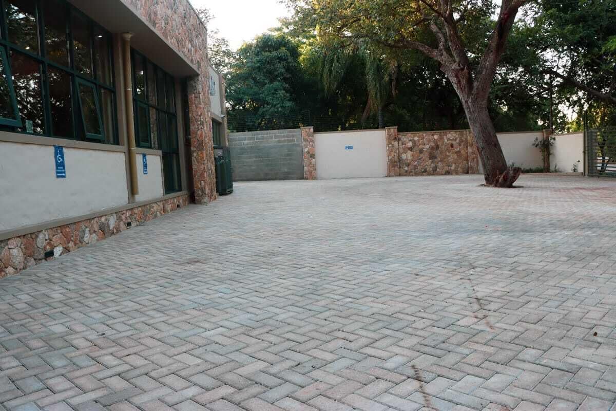 A paved courtyard with a building on one side, a tree, and a gate.