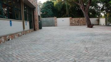 A paved courtyard with a building on one side, a tree, and a gate.