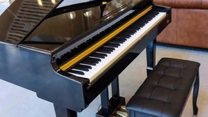 Un piano de cola en un amplio salón con pared de piedra y muebles modernos.