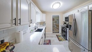 A modern kitchen with white cabinets, stainless steel appliances, and a tiled backsplash. - Kennesaw Komfort, Home for 8 (Kennesaw)