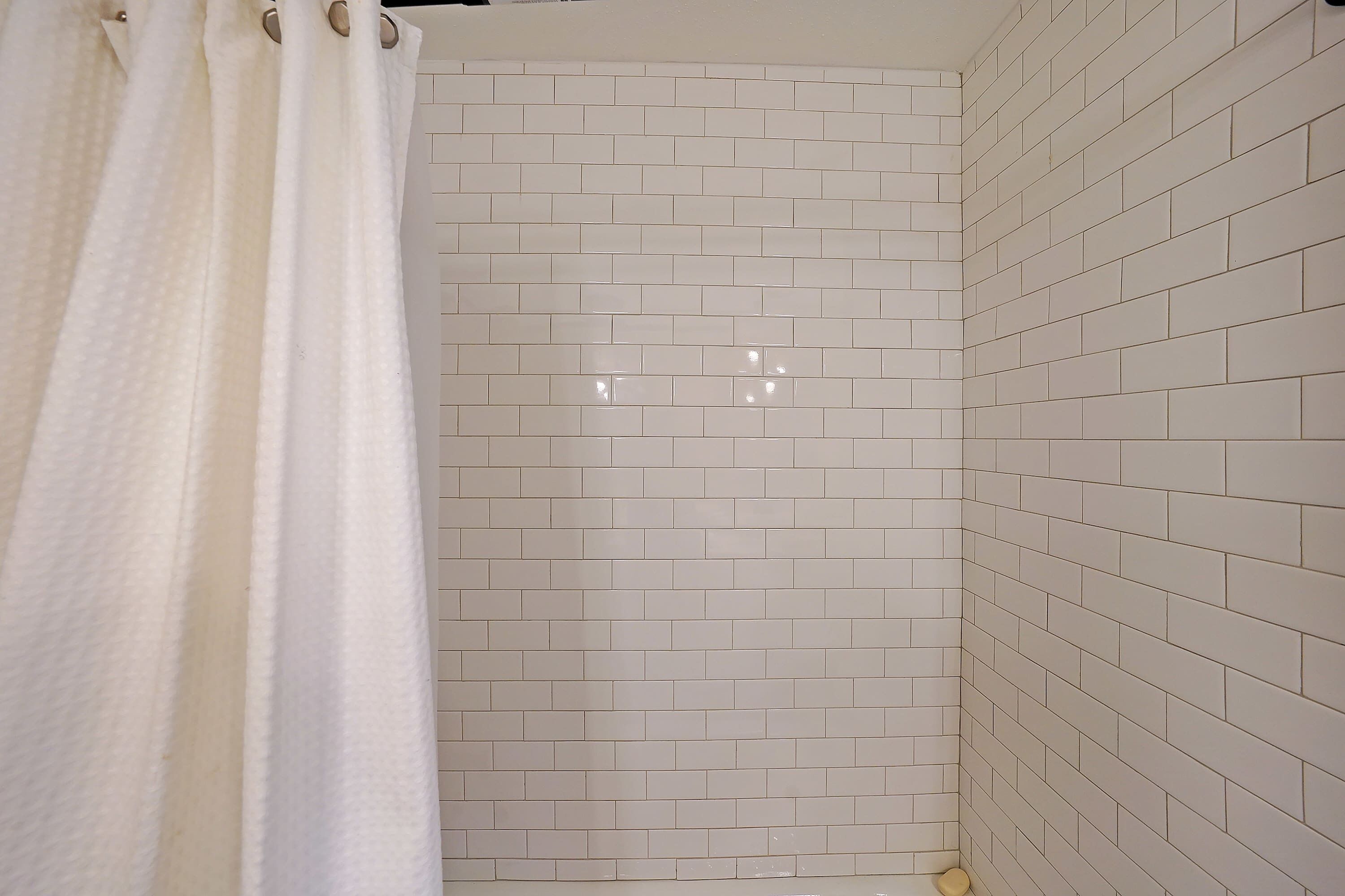 Un baño con azulejos blancos tipo metro, una cortina de ducha y un inodoro.