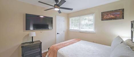 A bedroom with a bed, a nightstand, a TV, a ceiling fan, a window, and a door.