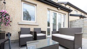 Eine Außenpatio-Terrasse mit Korbmöbeln, einem Glastisch und einer hängenden Blumenkomposition.