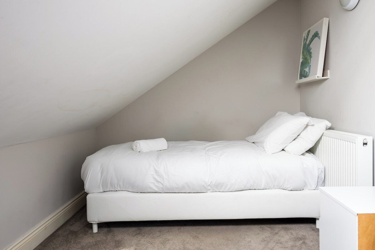 Una cama blanca en una habitación con techo inclinado y un radiador.