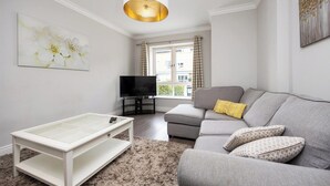 Ein modernes Wohnzimmer mit einem grauen Sofa, einem Flachbildfernseher, einem weißen Couchtisch und einem flauschigen Teppich.