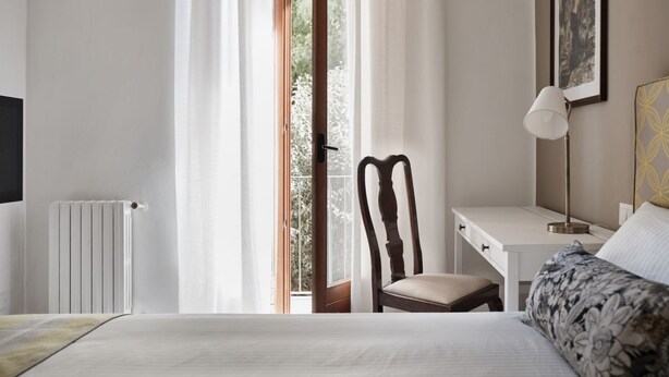 Een hotelkamer met een bed, een bureau, een stoel, een radiator en een raam met gordijnen.
