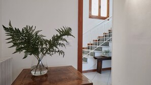 Een houten tafel met een varen in een glazen vaas, een trap en een witte muur.