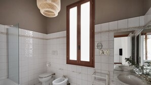 Een badkamer met een badkuip, twee toiletten, een bidet, een wastafelmeubel met een wastafel en een grote spiegel.
