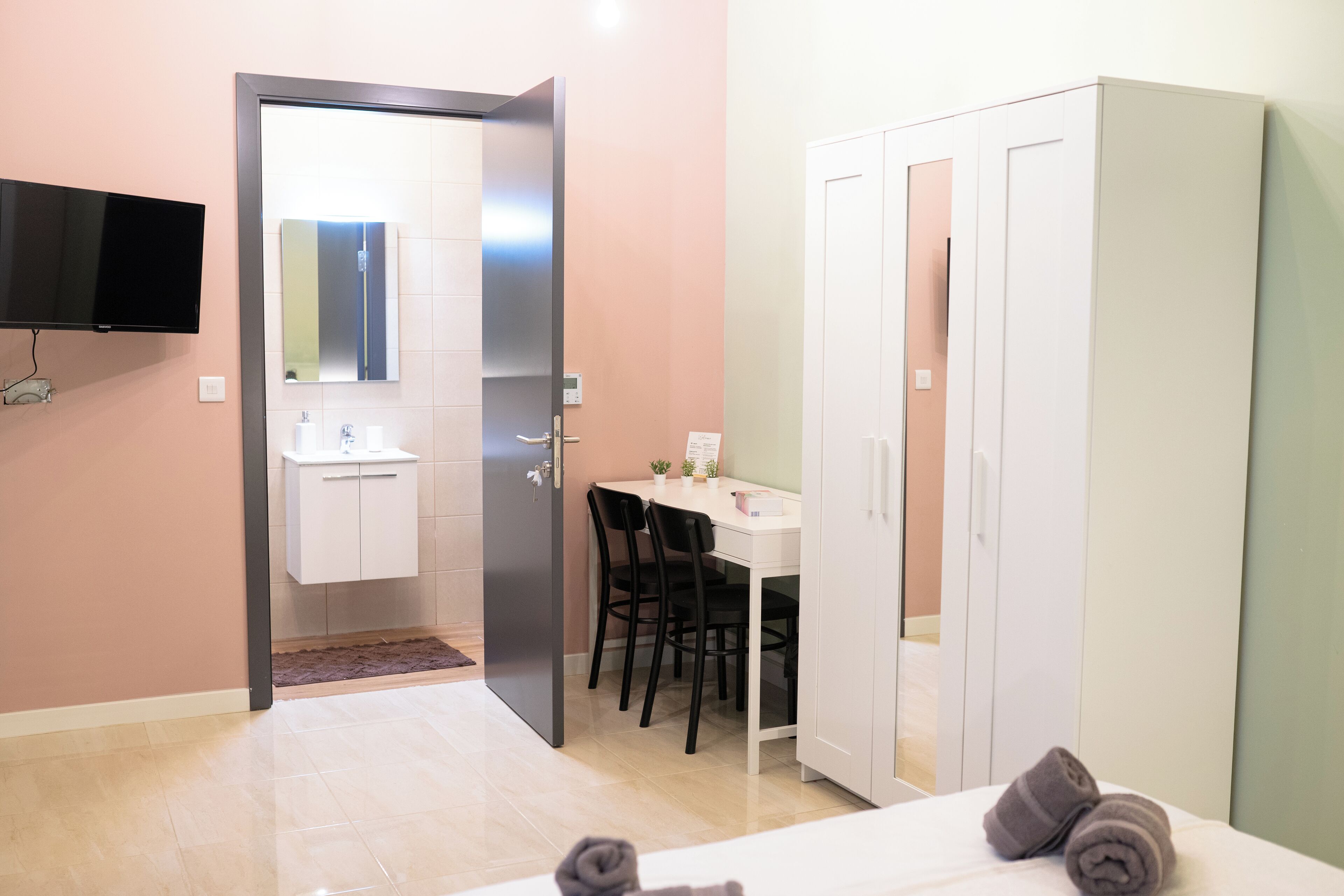 A modern hotel room with a bed, a desk, a chair, a wardrobe, a TV, and a bathroom.