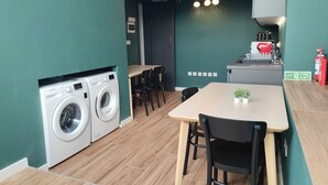 Een praktische keuken met een wasmachine, een eettafel met stoelen en een klein aanrecht met een spoelbak.